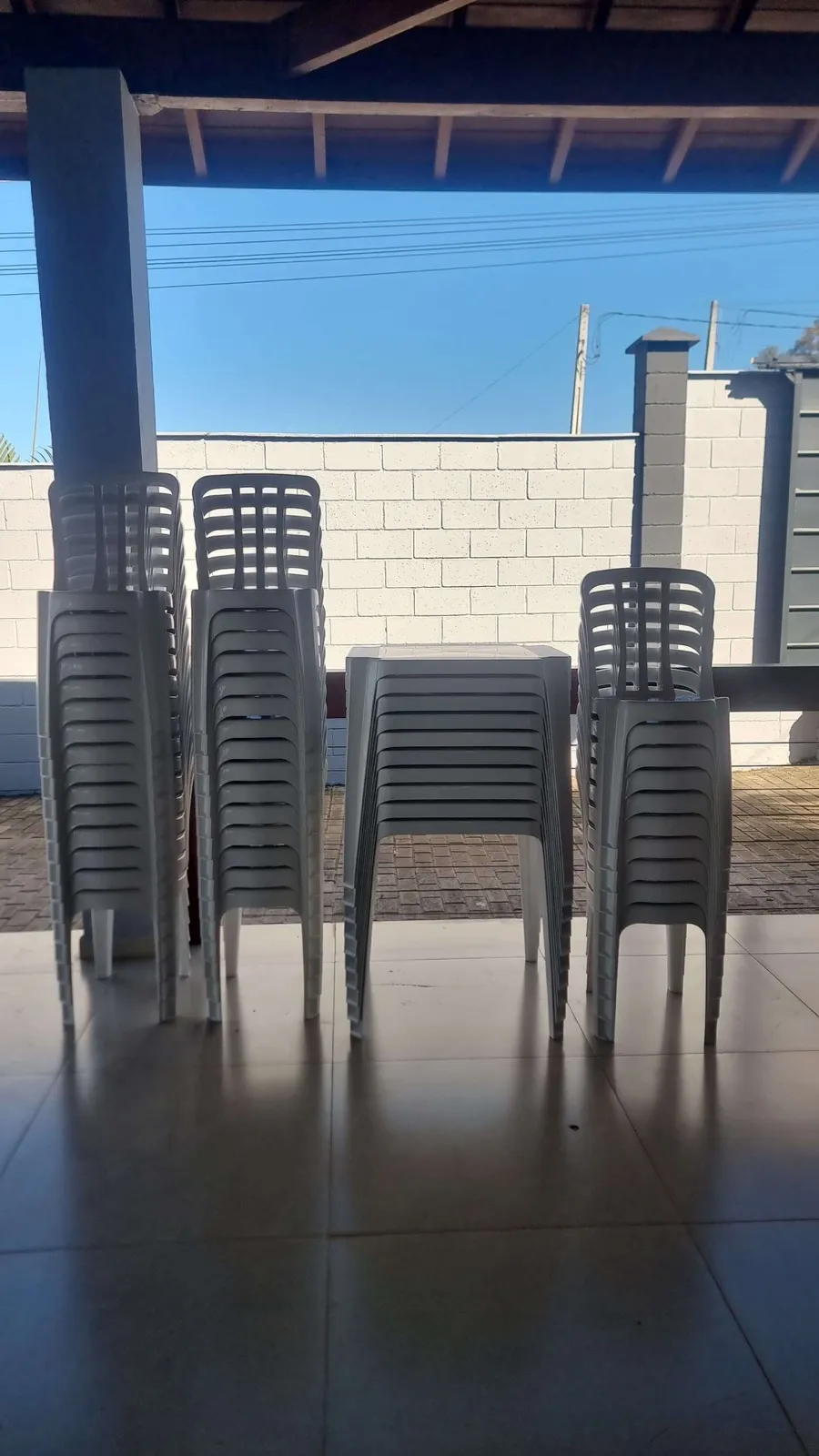 Mesas quadradas e cadeiras brancas empilhadas após entrega
